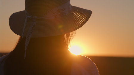 A woman is sitting comfortably, watching the beautiful sunset while wearing a stylish hatの写真素材
