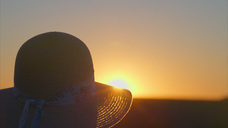 Embracing the Beauty of Sunset Serenity while Wearing a WideBrimmed Hat for Styleの写真素材