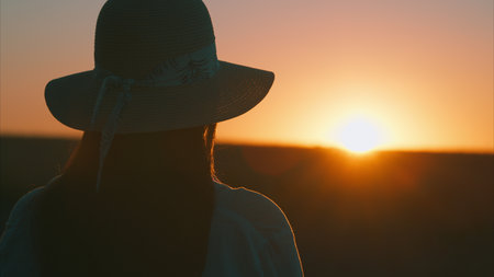 Experience the tranquil and peaceful moment of a beautiful sunset with a hatclad silhouetteの写真素材