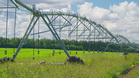 An Irrigation System Over Vibrant Green Fields Beneath a Cloudy Sky Filled with Cloudsの写真素材