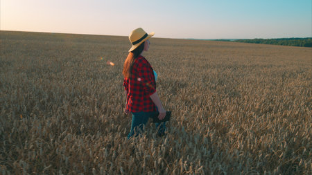 A woman gracefully walking through a vast golden wheat field as the sun sets in the sky