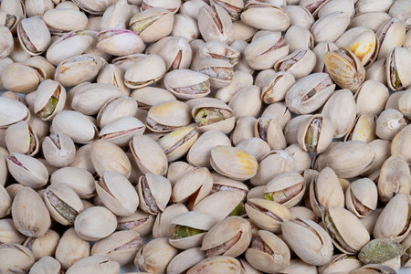 Pistachio shells scattered. Cracked shells display green kernels. Salted roasted pistachios with...