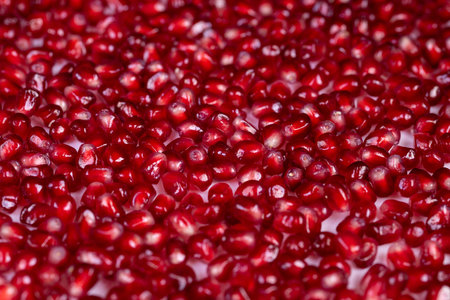 Bright pomegranate seeds arranged in repeating mosaic, smooth surface reflections create jewellike...