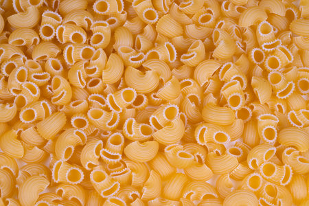 Closeup of dry pasta shells. Detailed shot of golden dry pasta shells with ridges. Dramatic macro...