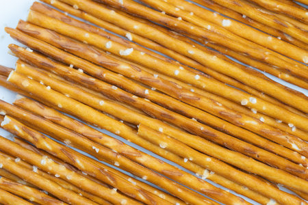 Salted pretzel sticks arranged neatly. Crunchy pretzels with coarse salt in orderly rows. Golden crisp pretzels sprinkled with salt crystals on plain backgroundの写真素材