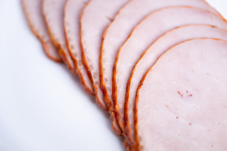 Closeup smoked meat slices arranged on white plate, soft lighting highlights delicate pink interior...