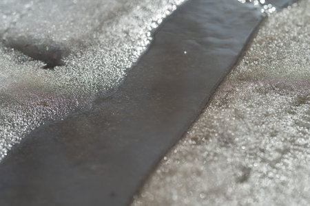 Glittering winter water stream scene. Radiant frozen brook flowing under sunlit highlights. Brilliant snowcovered creek with shimmering sunlight reflecting off icy surfacesの写真素材