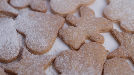 Powdered sugar dusted cookies closeup, assorted heart and star shapes on parchment, warm neutral...
