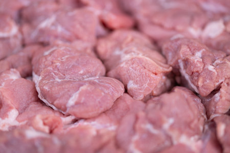 Fresh pork display. Marketready raw pork slices with moisture sheen on display. Dense cluster of trimmed raw pork pieces presented attractively under natural illuminationの写真素材