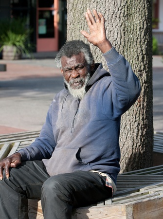 Elderly African American homeless man waving while sitting outdoorsの写真素材