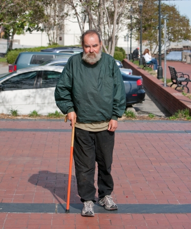 Handicapped homeless man walking with cane for support outdoors の写真素材