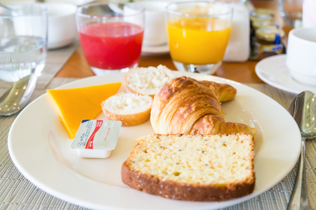 Bright close-up of a breakfast on the table in a cafe with a variety of fresh juices, croissant, cake, cheese and butter on the plateの写真素材