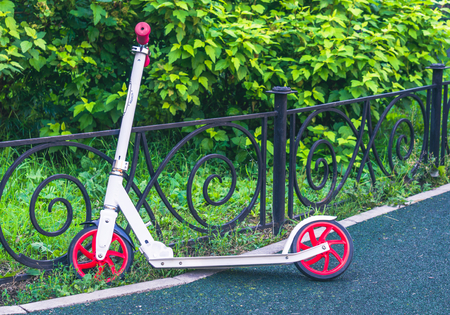 White and red scooter leaned on fence in parkの写真素材