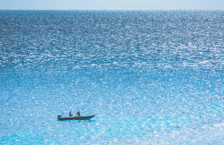 Distant motor boat with two people in it on the sparkling surface of the sea. Aerial view.