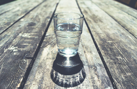 Close-up of one glass of clear water standing in middle of rough wooden table