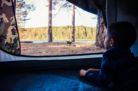 Little boy looking outside camping tent on the lake landscapeの写真素材