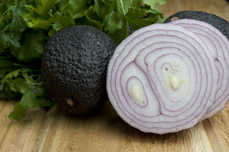 Two onion halves, avocados, and cilantro sit on a rough cedar plank.