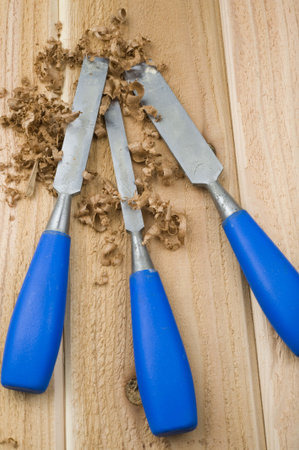 Three blue handled chisels sit on a rough cedar plank in a pile of wood shavings.