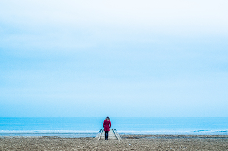 woman walking alone in the beach in winter evening with red dressの写真素材