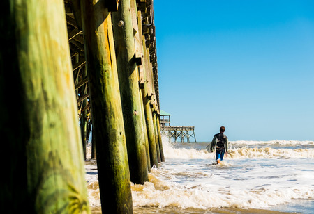 young man walking in the ocean with surfboard in floridaの写真素材