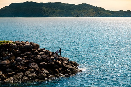 group of fishermen fishing on rock pier at sunset with calm blue sea の写真素材