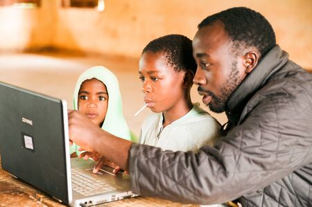 Bafoussam, Cameroon - 06 august 2018: young african children learn to use computer with young teacher touching screenのeditorial素材