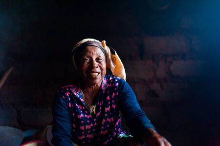 Douala Cameroon - 06 august 2018: closeup of old african lady in her rural home kitchen with traditional dress looking straight in camera with big smileのeditorial素材