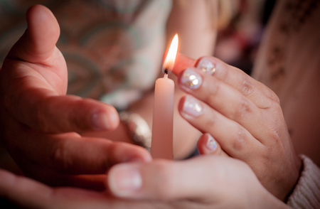 four hands of young people protecting fragile candle light fire as a metaphor of care and protection during religious ceremonyの写真素材