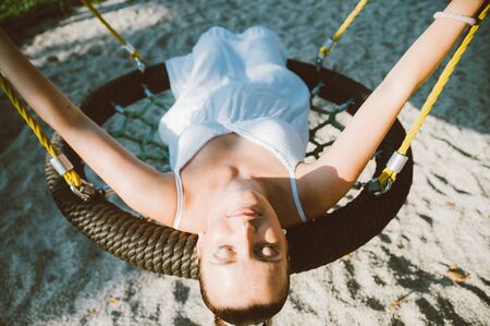 Milan, Italy - 20 july 2018: portrait of young expecting woman with white dress swinging in outdoors park expressing peace and serenityのeditorial素材