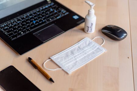 remote work kit on wooden office desk with hand sanitizer and face mask, a solution against the spread of corona virus for quarantined employeesの写真素材