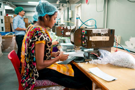 New delhi, India - 10 september 2019: an  indian woman at work using industrial equipment inside packaging manufacturing plant with serene expressionのeditorial素材