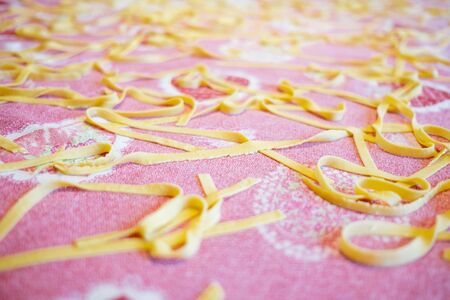 close up of yellow homemade fresh traditional italian tagliatelle pasta on white table cloth inside homeの写真素材