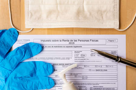 Barcelona, Spain - 20 april 2020: close up of impuesto sobre la renta form for spanish tax declaration with gloves and face mask as a symbol of coronavirus and spanish economyのeditorial素材