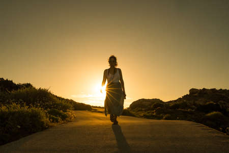 young determined woman silhouette walking against the sunset with sunrays, a beautiful evocative scene, symbol of following your own path and destinyの写真素材