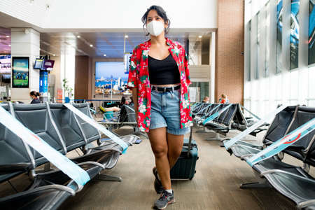 Barcelona, Spain - 20 august 2020: young woman walking inside airport wearing protective face mask with happy and positive attitude with trolley, holidays during the covid19 pandemicのeditorial素材