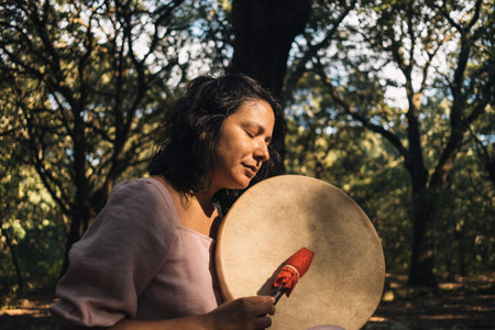 young woman playing tambour in the woods in nature with incense. mystic woman doing ritual and...
