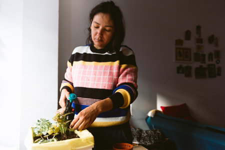 young woman watering plants in home made garden during lock down. taking care of plants at home spraying water with natural sun lightの写真素材