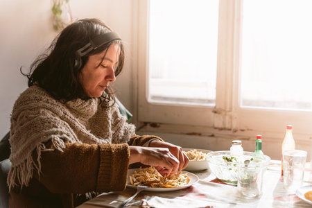 young single hispanic woman having lunch alone with tacos and chicken and guacamole, wearing headphones, at home. Cooking her own meal during lockdownの写真素材