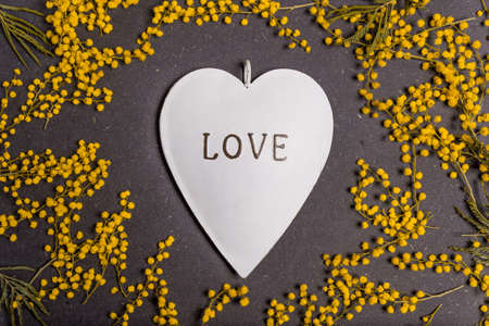 womens day concept, yellow mimosa flowers on black background with heart with love text. woman's day and 8 march concept.の写真素材