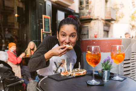 young woman eating bruschetta doing italian happy hour known as aperitivo in bar outdoor terrace. smiling and enjoying italian foodの写真素材