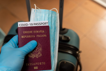 hand with latex gloves holding covid vaccine passport and face mask concept with luggage at airport....