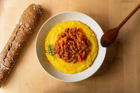 stewed chili beans with polenta on wooden table top view with bread. homemade traditional recipe with rosemary and red bell pepper with wood spoonの写真素材