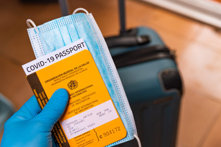 hand with latex gloves holding covid vaccine passport and face mask concept with luggage at airport....