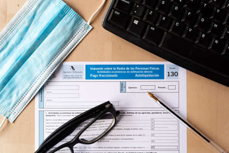 Madrid, spain - 3 march 2021: close up of "modelo 130" spanish income tax declaration form, symbol of spanish taxes and economy, with pen face mask and computer keyboard on tableのeditorial素材