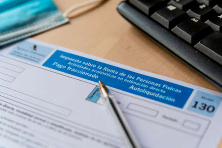 Madrid, spain - 3 march 2021: close up of "modelo 130" spanish income tax declaration form, symbol of spanish taxes and economy, with pen face mask and computer keyboard on tableのeditorial素材