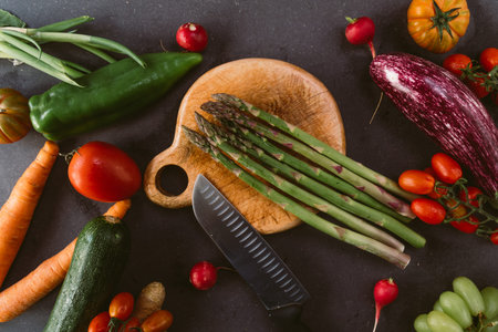 wood chopping board with asparagus rounded by springtime fresh vegetables like eggplant and carrots with soft light. concept of spring food and organic vegan nutritionの写真素材