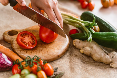 hand chopping tomato on wood preparing spring lunch with fresh vegetables like eggplant and carrots...