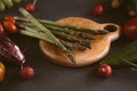 wood chopping board with asparagus rounded by springtime fresh vegetables like eggplant and carrots with soft light. concept of spring food and organic vegan nutritionの写真素材