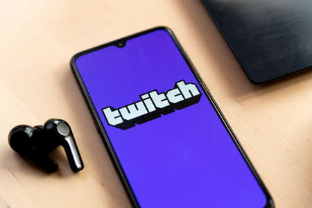 Barcelona, Spain - 20 april 2021: a mobile phone laying wood desk with Twitch live streaming app and earphone ready for live feed. Twitch is a popular live video appのeditorial素材