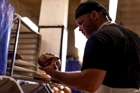 young baker in bakery holding bread and taking care of it with passion and care. concept of...